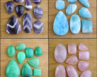 May include: A collection of polished gemstones in various shapes and colors. The image showcases amethyst, larimar, chrysoprase, and rose quartz stones. The stones are oval, teardrop, and square-cut, with shades of purple, blue, green, and pink.
