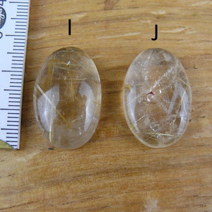 May include: Two oval-shaped, clear quartz stones with gold inclusions. The stones are about 2 inches long and are labeled "I" and "J".