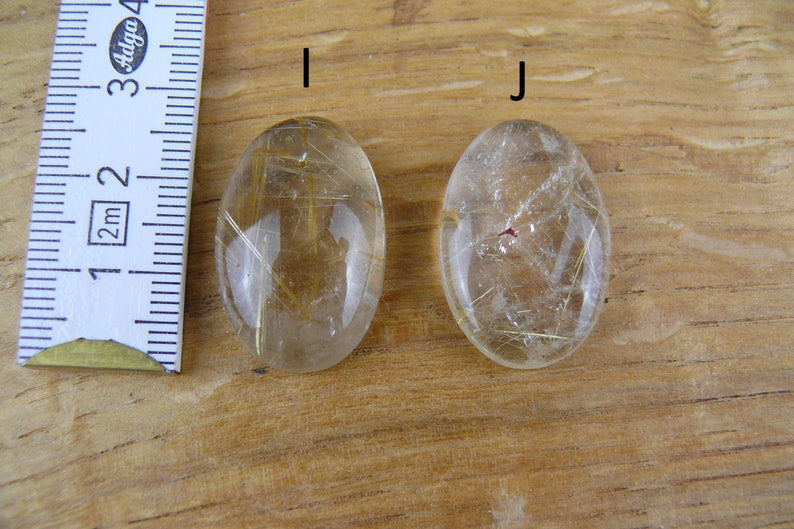 May include: Two oval-shaped, clear quartz stones with gold inclusions. The stones are about 2 inches long and are labeled "I" and "J".
