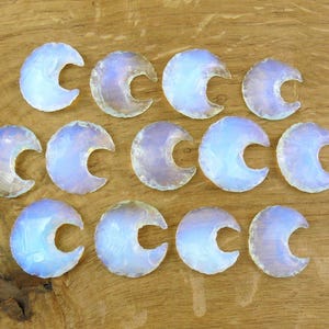 May include: A collection of opalescent crescent moon-shaped stones, arranged on a wooden surface. The stones have a translucent quality with hints of blue and purple. The wooden surface has a natural grain pattern.
