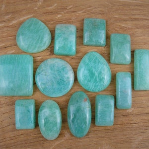 Può includere: Una collezione di 13 pietre preziose di amazonite verde, lisce e levigate, di varie forme e dimensioni. Le pietre sono disposte a forma di cuore su una superficie di legno.