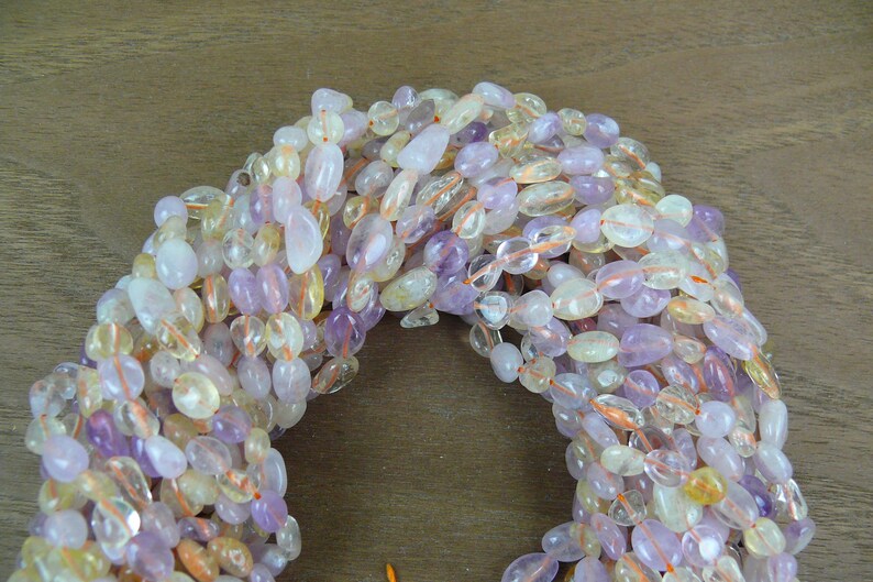 May include: A strand of mixed gemstone beads in shades of purple, yellow, and clear. The beads are oval shaped and have a smooth, polished finish.