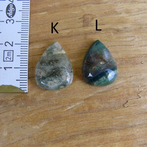 K&ouml;nnte beinhalten: Zwei tropfenf&ouml;rmige gr&uuml;ne Achat-Cabochons, beschriftet mit "K" und "L", werden neben einem Lineal gezeigt. Die Cabochons sind etwa 2,5 cm lang.