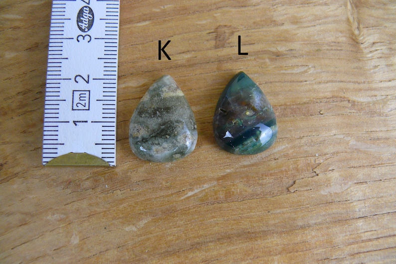 K&ouml;nnte beinhalten: Zwei tropfenf&ouml;rmige gr&uuml;ne Achat-Cabochons, beschriftet mit "K" und "L", werden neben einem Lineal gezeigt. Die Cabochons sind etwa 2,5 cm lang.