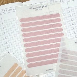 May include: Two sheets of washi tape with long rounded rectangular stickers. The top sheet has pink stickers with the text "LONG ROUNDED WASHI CORAL CLOUD". The bottom sheet has beige stickers with the text "LONG ROUNDED WASHI APRICOT CREAM".