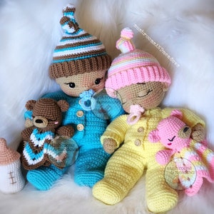 May include: Two crocheted baby dolls, one in a blue outfit and one in a yellow outfit, each holding a crocheted teddy bear. The dolls are wearing hats and have pacifiers in their mouths. The text "mushrooms & meadows" is visible in the image.