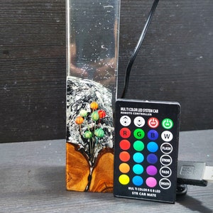 May include: A clear glass cylinder with a wooden base and a colorful, abstract design inside. The cylinder is lit from within by a multi-colored LED light system that can be controlled by a remote control. The remote control has buttons for red, green, blue, white, flash, strobe, fade, and smooth.