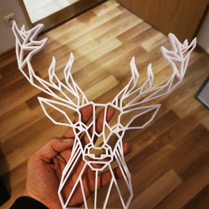 Puede incluir: Decoración de pared de cabeza de ciervo geométrico blanco hecha de plástico. La cabeza de ciervo es un diseño 3D con un patrón geométrico.