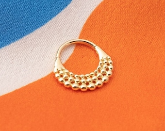 May include: Gold hoop earring with a beaded design. The earring is on a colorful fabric background.