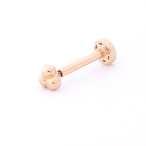 Pode incluir: Joia corporal de ouro com uma pequena extremidade em forma de flor e um verso plano.