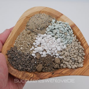 Könnte beinhalten: Eine Holzschale gefüllt mit verschiedenen Arten von Erde und Kies, darunter weißer Bims, grauer Kies, braune Erde und beiger Sand. Die Schale wird in einer Hand gehalten.