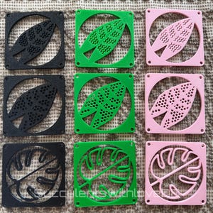 Può includere: Un set di nove sottobicchieri quadrati disposti in una griglia tre per tre. I sottobicchieri sono neri, verdi e rosa, ognuno con un ritaglio circolare contenente un diverso motivo a foglia, tra cui texture, puntini e foglie di monstera.