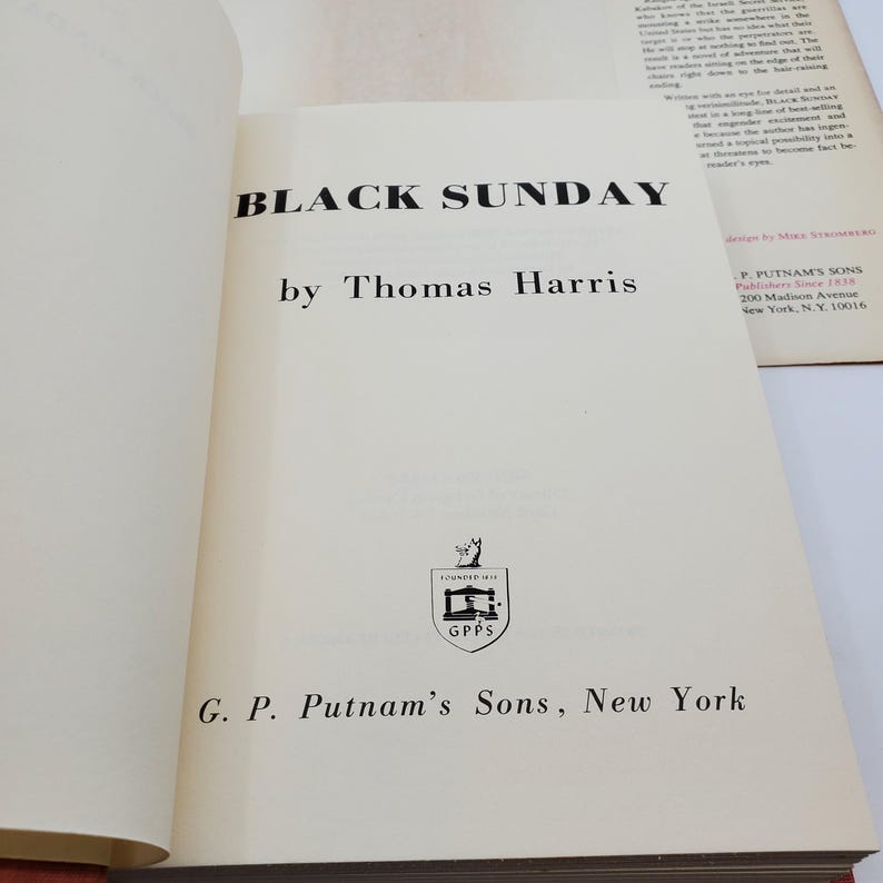 May include: An open book displaying the title "BLACK SUNDAY" by Thomas Harris. The text is in black on a cream-colored page. The publisher's details, including G. P. Putnam's Sons, New York, are also visible.