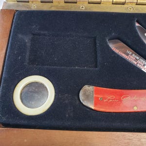 Puede incluir: Una caja de madera con interior de terciopelo negro, que contiene un peque&ntilde;o espejo y dos cuchillos. Un cuchillo tiene un mango rojo con la firma "Lou Gehrig". El otro cuchillo tiene el texto "The Iron Horse 1903-1941 2130 Consecutive Games."