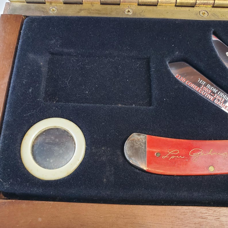 Puede incluir: Una caja de madera con interior de terciopelo negro, que contiene un peque&ntilde;o espejo y dos cuchillos. Un cuchillo tiene un mango rojo con la firma "Lou Gehrig". El otro cuchillo tiene el texto "The Iron Horse 1903-1941 2130 Consecutive Games."