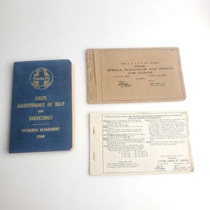 May include: An image of three vintage documents. A blue book titled "Rules Maintenance of Way and Structures" with "Santa Fe" logo. A tan booklet titled "Spirals, Elevations and Speeds for Curves". A white sheet titled "String Lining of Curves".