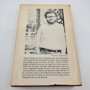 May include: A book cover with a black and white photograph of a man with glasses and a beard. The text provides biographical details about Thomas Harris and mentions "BLACK SUNDAY". The cover is aged.
