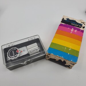 May include: A vintage Polaroid Self Timer #192 and its original box. The timer is in a clear plastic case. The box is rectangular with a rainbow color scheme.