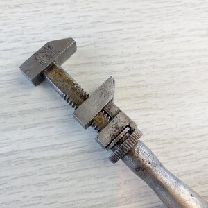 Puede incluir: Una llave inglesa ajustable vintage con acabado plateado y el texto "GEM MFG. & CO." en el mango.