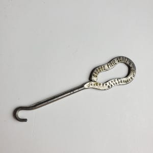 May include: Vintage metal shoe button hook with a curved handle and a hook on the end. The handle is stamped with the text "CARSON PIRIE SCOTT & CO. DISTINCTIVE FOOTWEAR". The hook is silver-toned.