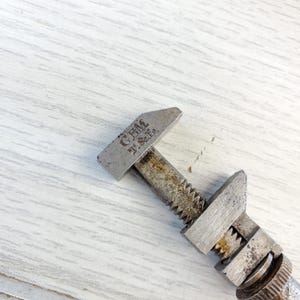 Puede incluir: Una llave inglesa de plata ajustable con el texto "GEM J. & E. Co." en la parte superior. La llave est&aacute; sobre una superficie de madera blanca.