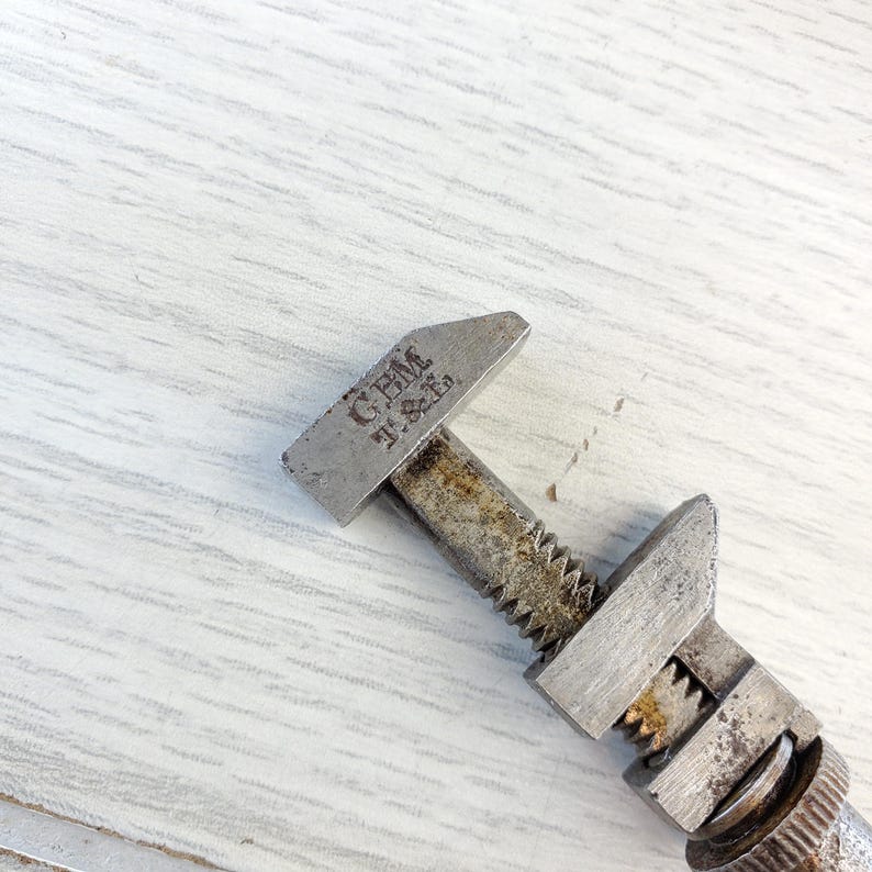 Puede incluir: Una llave inglesa de plata ajustable con el texto "GEM J. & E. Co." en la parte superior. La llave est&aacute; sobre una superficie de madera blanca.