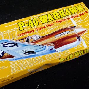 May include: A yellow box for a P-40 Warhawk model kit. The box features an illustration of the airplane in brown and silver, with text that reads "Legendary 'Flying Tiger' Fighter of World War 2."
