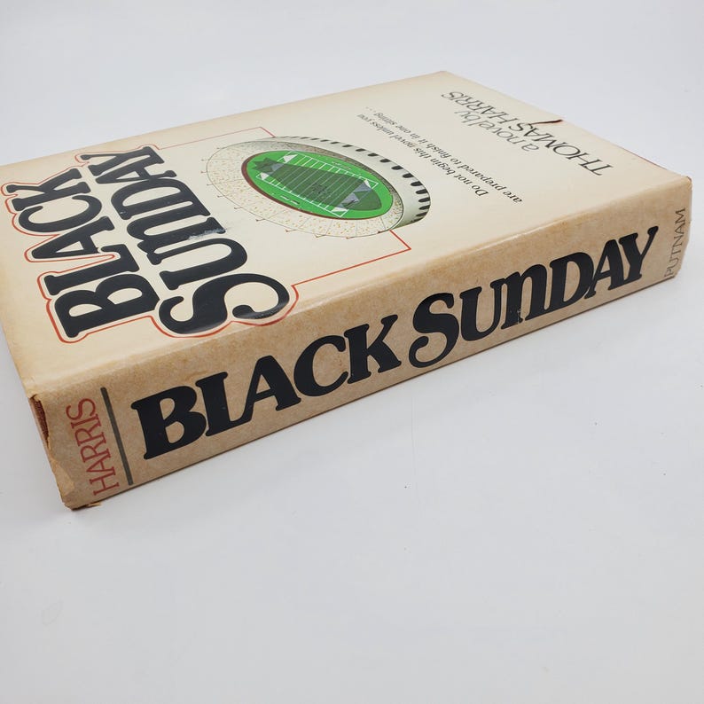May include: A vintage hardcover book, "Black Sunday" by Thomas Harris. The cover is a tan colour with bold black lettering. The book features a stadium graphic and the author's name. The publisher's name is also visible.