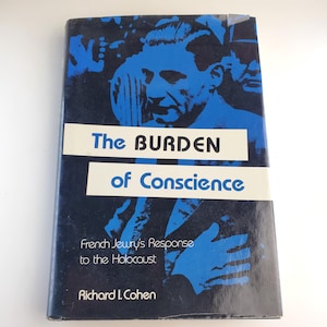 May include: A hardcover book titled "The Burden of Conscience" with a blue and black cover. The cover features a blue illustration of a man's face and hands, with the title in white text. The subtitle reads "French Jewry's Response to the Holocaust."