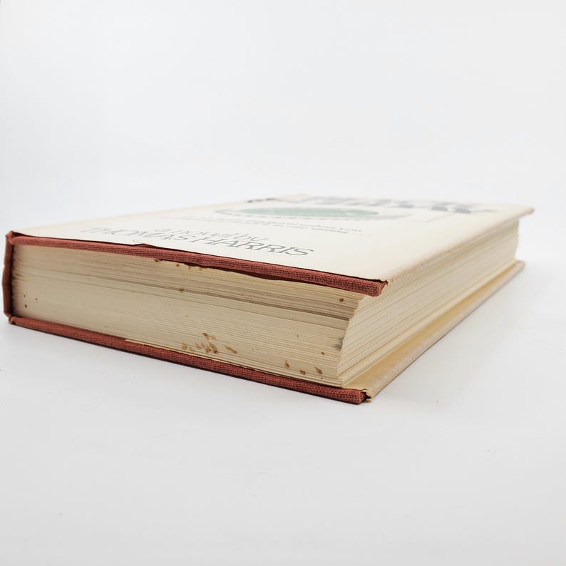 May include: A hardback book with a beige cover and a red spine. The title and author's name are printed on the cover. The book's pages are visible, and the edges show some wear. The book is lying on a white surface.