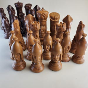 May include: A collection of wooden chess pieces in shades of brown. The set includes various pieces like pawns, rooks, knights, bishops, a queen, and a king. The pieces are intricately carved with detailed features, showcasing a classic chess set design.