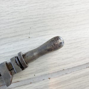 Puede incluir: Una llave inglesa de plata con un mango desgastado. La llave es de metal y tiene un agarre texturizado.