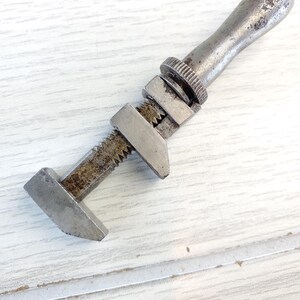 Puede incluir: Una llave inglesa de plata con un mango desgastado. La llave tiene una mand&iacute;bula dentada y un tornillo de ajuste roscado.