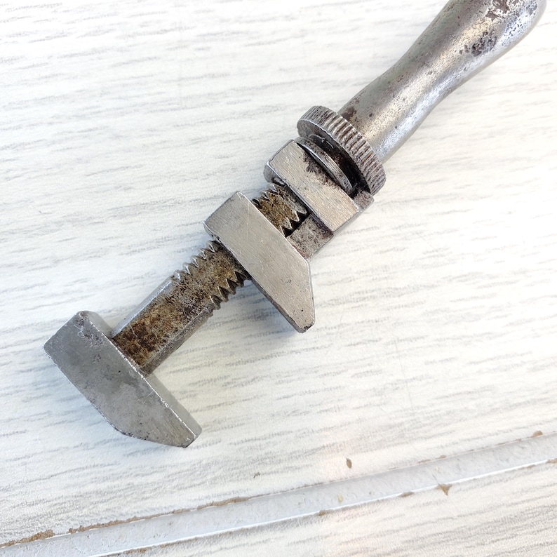 Puede incluir: Una llave inglesa de plata con un mango desgastado. La llave tiene una mand&iacute;bula dentada y un tornillo de ajuste roscado.
