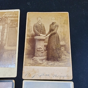 May include: Sepia-toned photograph featuring a man and woman standing together. The man wears a suit and the woman a long dress. They stand near a decorative column. The photograph is labeled "R. J. Stone, Photographer."
