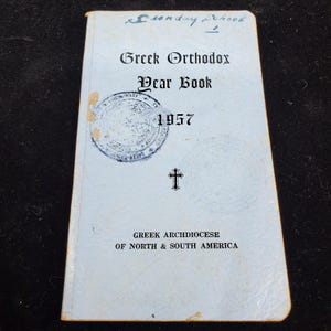 May include: A light blue Greek Orthodox Year Book from 1957. The cover features the text "Sunday School" in cursive, the title, a cross, and a circular seal. The book is from the Greek Archdiocese of North & South America.