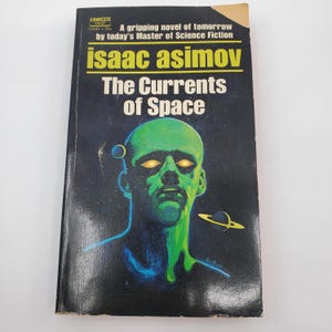 May include: A vintage paperback book titled "The Currents of Space" by Isaac Asimov. The cover features a green-skinned alien with glowing eyes against a dark, starry background. The book has a yellow and black title banner.