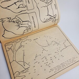 Op de afbeelding: Een zwart-witte verbind-de-stippen-activiteitenboekpagina met een berggeit, een gorilla en een poema op de omslag. De pagina bevat een verbind-de-stippen-illustratie van een boom en een berglandschap. De instructies luiden: "Beweeg je potlood van stip naar stip van 1 tot 63 en heel snel zul je voor je ogen duidelijk het grootste dier in heel het land tot leven zien komen terwijl je je hand beweegt."