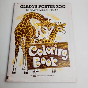 May include: A vintage coloring book featuring two giraffes with a wooden sign that reads "Coloring Book". The book is titled "Gladys Porter Zoo Brownsville, Texas".