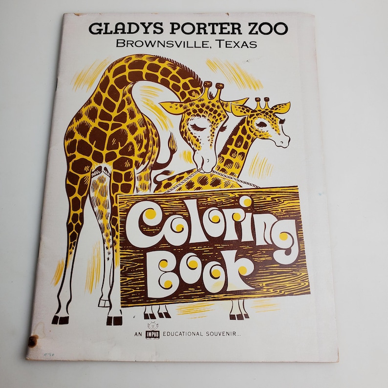 Op de afbeelding: Een vintage kleurboek met twee giraffen en een houten bord met de tekst "Coloring Book". Het boek heeft de titel "Gladys Porter Zoo Brownsville, Texas".