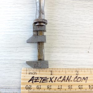 Puede incluir: Una llave inglesa de plata ajustable con el texto "THE RED" en el mango. La llave se mide contra una regla de madera con marcas en pulgadas.