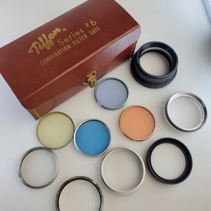 May include: A brown leather case with the text "Tiffen Series #6 Combination Filter Safe" on the top. The case is open and contains a variety of round filters in different colors, including blue, orange, yellow, and gray.
