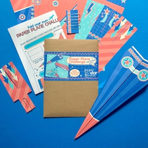 May include: A paper aeroplane craft kit with instructions and colourful paper. The kit includes a brown envelope with the text "Paper Plane Challenge Fun to Fold & Fly" and "Bonus Helicopters to Make". The paper is decorated with stars and stripes.