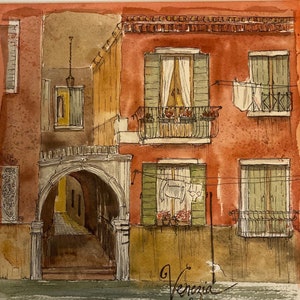 May include: Watercolor painting of a red building with a stone archway and windows with green shutters. The building has a balcony with flowers and laundry hanging on a clothesline. The painting is signed "Venezia" in the bottom right corner.