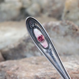May include: A silver spoon with a pink and white design and a pink rhinestone in the centre.