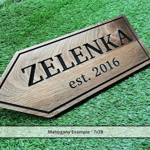 May include: A wooden sign with the name "ZELENKA" and the year "est. 2016" engraved in black. The sign is arrow-shaped and made of mahogany wood. The sign measures 7x18 inches.