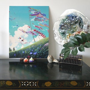 Könnte beinhalten: Ein schwarzer Holztisch mit einem farbenfrohen Gemälde eines Feldes mit Drachen, die am Himmel hängen. Auf dem Tisch stehen eine rote Kerze in einem schwarzen Kerzenleuchter, ein kleiner Abakus und eine Glaskugel.