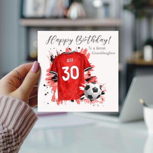 K&ouml;nnte beinhalten: Geburtstagskarte mit dem Text "Happy Birthday! To a Special Granddaughter." Die Karte zeigt ein rotes Fu&szlig;balltrikot mit dem Namen "JESS" und der Nummer "30" sowie einen Fu&szlig;ball. Der Hintergrund hat rote und schwarze Farbspritzer.