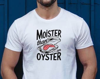 May include: White t-shirt with the text "Moister than an Oyster" in black, featuring an oyster graphic with pink and white details. The shirt is short-sleeved and worn by a person wearing glasses and a watch.