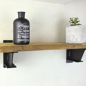 Könnte beinhalten: Ein Holzregal mit schwarzen Metallkonsolen. Das Regal ist mit einer schwarzen Glasflasche mit dem Text "Happy is what happens when all your dreams come true" und einer kleinen Topfpflanze dekoriert.